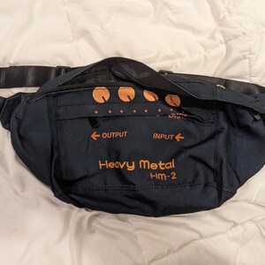 May include: A black fanny pack with an orange graphic that says "Heavy Metal HM-2". The pack has a zippered pocket and an adjustable strap.