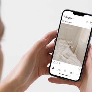 A visual of person holding a phone in two hands displaying an Instagram post that reads "Begin with less pressure" over a soft bedroom photograph, showing how the template appears on a real Instagram feed.