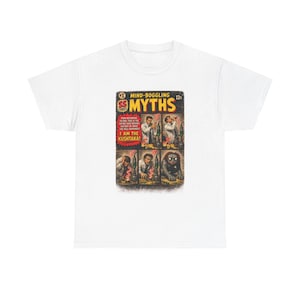 May include: A white t-shirt featuring a graphic print of a vintage comic book cover titled Mind-Boggling Myths. The comic art depicts a scientist in a lab transforming into a creature, with text reading I Am The Kushtaka and SS Comics.