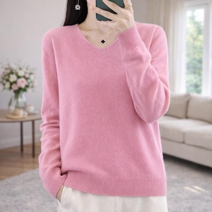 Peut inclure: Un pull rose clair à col en V et manches longues. Le pull a des poignets et un ourlet côtelés. Le tricot doux est de couleur unie et semble être fait d'une matière chaude. Le pull est de style classique.