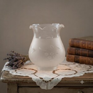 May include: A frosted glass lamp shade with a ruffled top edge and a subtle etched pattern of grapes and leaves. The shade features a translucent finish that transitions to a clearer glass at the top, showcasing a delicate and smooth texture.