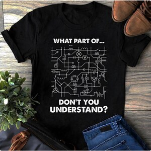 May include: Black t-shirt with a white circuit diagram design and the text "WHAT PART OF... DON'T YOU UNDERSTAND?". The shirt also features a pair of brown leather boots and blue jeans.