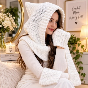 Può includere: Una sciarpa con cappuccio all'uncinetto bianco con muffole integrate, caratterizzata da un motivo a punti testurizzato e un design a cappuccio a punta. L'accessorio è realizzato in filato spesso e copre testa, collo e mani in un unico pezzo.