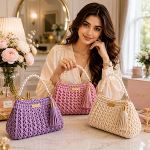 May include: Three crochet handbags in purple, pink, and cream, each featuring a textured knit pattern, a gold-toned metal brand plaque, a matching leather tassel, and a handle made of white faux pearls with gold-toned metal hardware attachments.