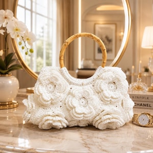 Könnte beinhalten: Eine weiße Häkeltasche mit einem strukturierten Blumenmuster auf der Außenseite und einem runden Bambusgriff. Die Tasche ist aus mehreren geschichteten, dreidimensionalen gehäkelten Blumenmotiven gefertigt, die eine dichte, dekorative Oberfläche bilden.