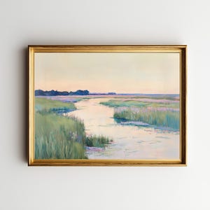 Puede incluir: Pintura de paisaje enmarcada que representa una escena de marisma. La obra presenta una vía fluvial que serpentea a través de altas hierbas verdes y plantas de color lavanda bajo un cielo suave y pastel. La pintura está encerrada en un marco dorado.