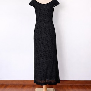 May include: A black, full-length dress with a scoop neckline and short sleeves. The dress is made of a textured fabric and is displayed on a mannequin against a white background.