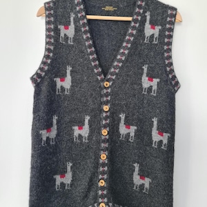 May include: A grey button-up vest featuring a repeating pattern of grey llamas with red saddle blankets. The vest has a V-neck, wooden buttons, and a red and grey patterned trim around the edges.