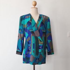 Könnte beinhalten: Ein Vintage-Blazer mit einem geometrischen Muster in Türkis-, Blau-, Grau- und Olivgrüntönen. Der Blazer hat ein doppelreihiges Design mit einem Reverskragen und langen Ärmeln. Der Stoff hat einen seidigen Glanz.