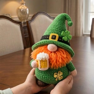 May include: A handmade crochet gnome in green, orange, and tan, holding a mug of beer. The gnome wears a green hat with a black band and gold buckle, and a shamrock. The gnome has an orange beard and a gold shamrock on its chest.