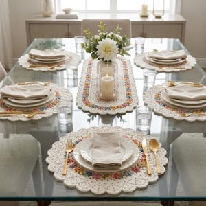 Puede incluir: Una mesa de comedor para seis personas con platos blancos, cubiertos dorados y servilletas de lino. La mesa está adornada con manteles individuales y un camino de mesa de ganchillo, con estampados florales en colores pastel. Un jarrón de flores blancas y velas completan el ambiente.