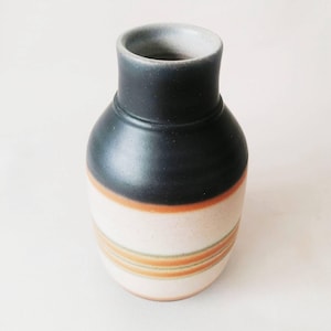 May include: A ceramic vase with a dark navy blue top and a cream-coloured body. The body features horizontal bands of orange and green stripes. The vase has a rounded shape and a narrow neck, suitable for displaying flowers or as a decorative item.