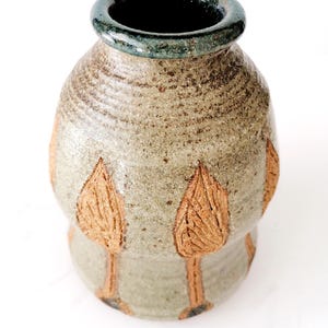 May include: A handcrafted ceramic vase with a textured, earthy appearance. The vase features a light brown and green color scheme, with a dark green rim and embossed leaf designs. The vase is approximately 6 inches tall.