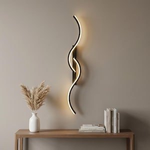 Könnte beinhalten: Eine moderne Wandleuchte mit schwarzem Rahmen und geschwungenem Design. Die Leuchte hat einen warmweißen Schein und ist an einer neutralfarbenen Wand montiert. Die Leuchte ist ein dekoratives Beleuchtungselement.