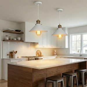 May include: Two white pendant lights with brass accents hang above a kitchen island. The lights have a conical shade and exposed Edison-style bulbs. The kitchen features white cabinets, a wooden island, and a light-colored countertop.