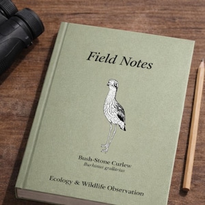 May include: A green Wildlife Field Journal with the text "Field Notes" and "Ecology & Wildlife Observation." The journal features a Bush-Stone Curlew illustration. A pencil and binoculars are visible.