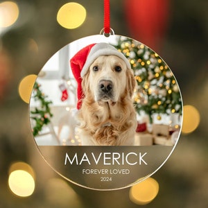 May include: A round, clear, acrylic Christmas ornament with a photo of a golden retriever wearing a Santa hat. The ornament has the text "Maverick Forever Loved 2024" printed on it.