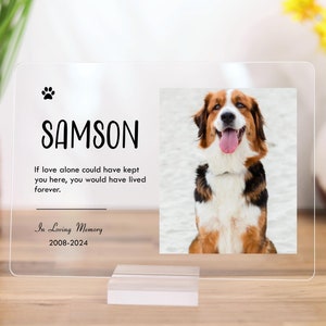 May include: A clear acrylic pet memorial plaque with a photo of a brown and white dog. The plaque has the name "SAMSON" and the text "If love alone could have kept you here, you would have lived forever." It also includes the text "In Loving Memory 2008-2024".