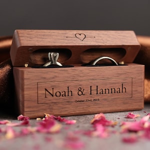 May include: A wooden ring box with two compartments for rings. The box is engraved with the names "Noah & Hannah" and the date "October 22nd, 2023".