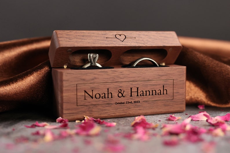 May include: A wooden ring box with two compartments for rings. The box is engraved with the names "Noah & Hannah" and the date "October 22nd, 2023".
