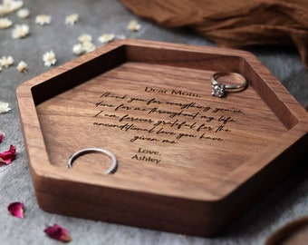 May include: A hexagonal wooden ring dish with a personalized message engraved on the surface. The message reads: "Dear Mom. Thank you for everything you've done for me throughout my life. I am forever grateful for the unconditional love you have given me. Love, Ashley."