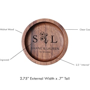 May include: A round wooden ring dish with a deep engraved design. The dish is made of genuine walnut wood and has a clear coat finish. It features the initials "SL" with a floral design and the text "SHANE & LAUREN 10-18-2024". The dish measures 2.75 inches in diameter and is 0.7 inches tall. The internal width is 2.3 inches.