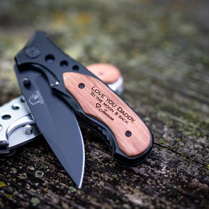 May include: A black pocket knife with a wooden handle engraved with the message "Love you Daddy, to the moon & back." The handle is also engraved with a heart and the name "Jessie".
