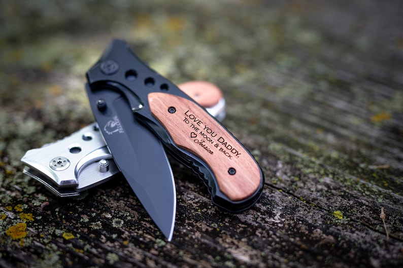 May include: A black pocket knife with a wooden handle engraved with the message "Love you Daddy, to the moon & back." The handle is also engraved with a heart and the name "Jessie".