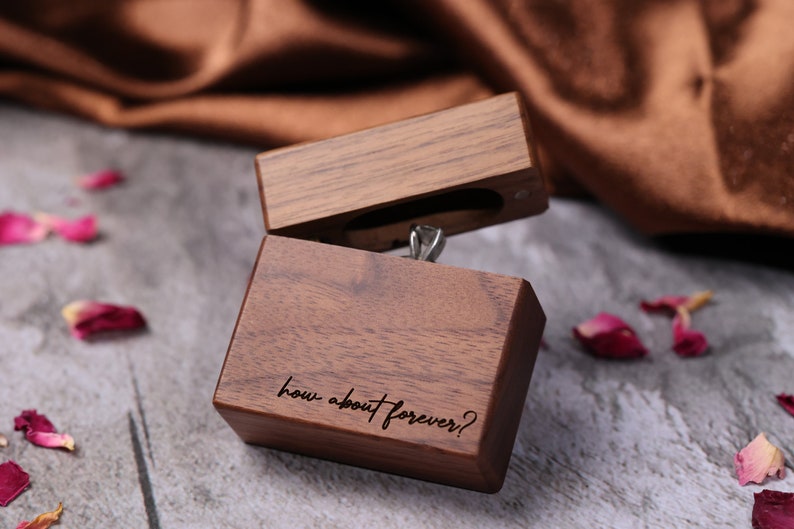 May include: A wooden ring box with the inscription "how about forever?" on the front. The box is open and a silver ring is visible inside.
