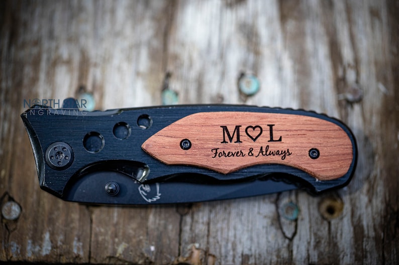 May include: A black pocket knife with a wooden handle engraved with the initials "M&hearts;L" and the text "Forever & Always".