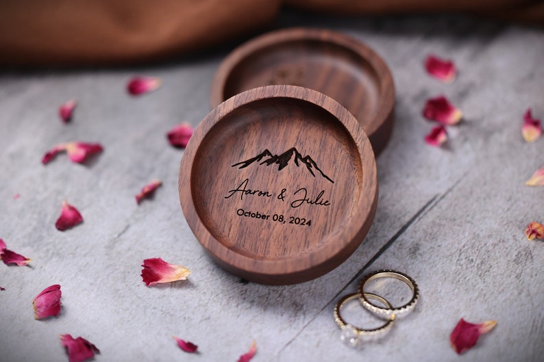 May include: A wooden ring box with a mountain range design and the text "Aaron & Julie October 08, 2024".