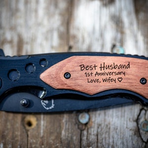 May include: A black pocket knife with a wooden handle engraved with the text "Best Husband 1st Anniversary Love, wifey".