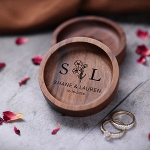 May include: A wooden ring box with a floral design and the initials "S" and "L" engraved on the lid. The box also has the text "Shane & Lauren 10-18-2024" engraved on the lid.