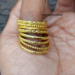 Könnte beinhalten: Ein Stapel goldfarbener Ringe mit verschiedenen geprägten Mustern. Die Ringe sind auf einem Finger gestapelt und zeigen die verschiedenen Designs und Texturen. Die Ringe scheinen aus Metall zu sein und haben ein glänzendes Finish. Der Shop-Name "ASHWANIJEWELLERSSSHOP" ist sichtbar.