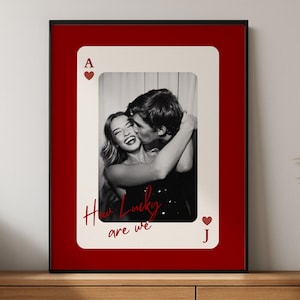 May include: A framed print featuring a black and white photograph of a couple embracing, set against a playing card design. The card is red with the text "How Lucky are we" and the Ace of Hearts and Jack of Hearts symbols.