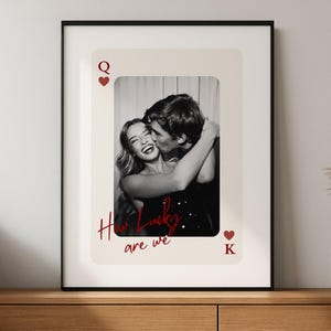 Peut inclure: Photographie encadrée en noir et blanc d'un couple s'embrassant, sur un fond de carte à jouer. La carte présente une Dame de Cœur et un Roi de Cœur, avec le texte "How Lucky are we" en script rouge.