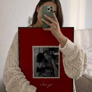 K&ouml;nnte beinhalten: Ein gerahmtes Foto mit rotem Hintergrund und schwarzem Rand. Das Foto im Inneren ist ein Schwarz-Wei&szlig;-Bild von zwei sich umarmenden Personen. Die Worte "i love you" sind unten in Kursivschrift geschrieben.