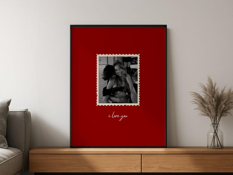 May include: A framed print with a black border and a red background. A black and white photo of two people hugging is in the center, framed like a postage stamp. The words "i love you" are written in cursive below the photo.