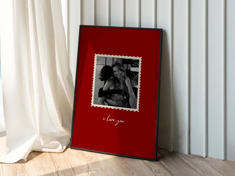 K&ouml;nnte beinhalten: Ein gerahmter Druck mit schwarzem Rahmen. Der Druck hat einen roten Hintergrund mit einem Schwarz-Wei&szlig;-Foto im Poststempelstil. Die Worte "i love you" sind darunter in Kursivschrift geschrieben.