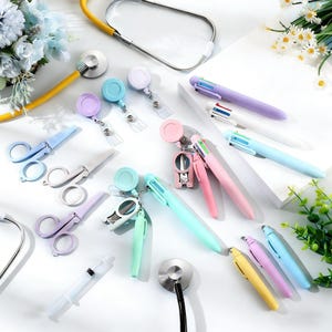 May include: A collection of medical equipment, featuring a yellow stethoscope, multi-coloured pens, badge reels, and small scissors. The pens have multiple ink colours. The items are arranged on a white surface with floral decorations.