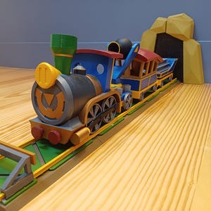 Peut inclure: Un train jouet coloré avec une locomotive bleue, rouge et jaune et un wagon assorti. Le train est sur une voie ferrée menant à un tunnel jaune. Le jouet est en plastique et présente un design détaillé.