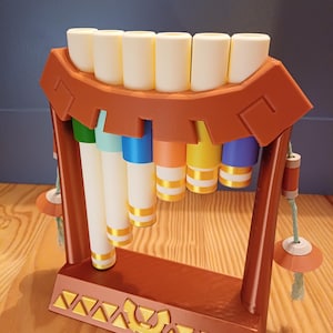 Può includere: Ocarina stampata in 3D di colore marrone caldo con un design decorativo. Lo strumento presenta sette cilindri bianchi sulla parte superiore e sei tubi colorati sottostanti, ciascuno con bande dorate. L'ocarina è uno strumento musicale.