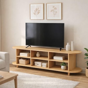 May include: A light wood TV stand with a black screen television on top. The stand has open shelving with decorative items. A sofa, coffee table, and rug are in the living room. Two framed botanical prints hang on the wall.