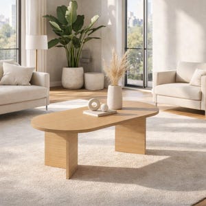 May include: A modern living room featuring a light beige sofa, armchair, and a wooden oval coffee table. The room is decorated with large potted plants, a cream-colored rug, and a vase with dried flowers. The room has large windows.