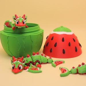 May include: A whimsical, green watermelon-shaped container with a red and green dragon figurine inside. The container is open, revealing the dragon. A red and green watermelon-shaped lid sits nearby, along with several watermelon-themed figurines.