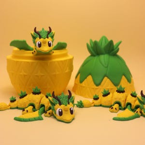 May include: A yellow and green articulated dragon figurine with pineapple-themed textures, featuring a matching pineapple-shaped container with a removable lid. The dragon has a segmented body, small wings, and dark brown horns, displayed alongside its shell.