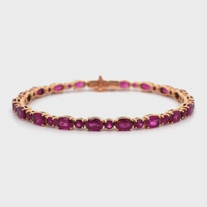 Op de afbeelding: Een roségouden armband met ovaal geslepen, dieproze edelstenen. De edelstenen zijn dicht op elkaar geplaatst, waardoor een doorlopende lijn ontstaat. De armband heeft een veilige sluiting en is ontworpen voor dagelijks gebruik.