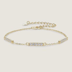 May include: A gold-coloured bracelet featuring three rectangular bars set with clear crystals. The bracelet has a fine chain and an adjustable clasp. The jewellery is presented against a soft, neutral background.