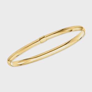 May include: A gold-colored bangle bracelet with a hinged clasp. The bracelet has a smooth, polished surface and a rounded shape. The clasp is a small, rectangular piece that connects the two ends of the bracelet. The bracelet is approximately 2.5 inches in diameter.