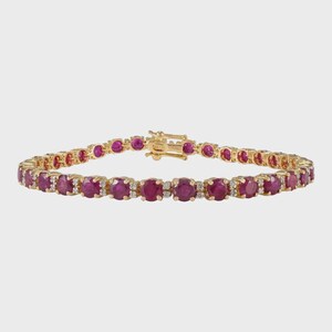 Puede incluir: Una pulsera dorada con una serie de piedras preciosas redondas de color rojo intenso, probablemente rubíes, y pequeñas piedras preciosas transparentes. La pulsera tiene un cierre seguro y está engastada en un engaste de metal dorado. Las piedras están espaciadas.